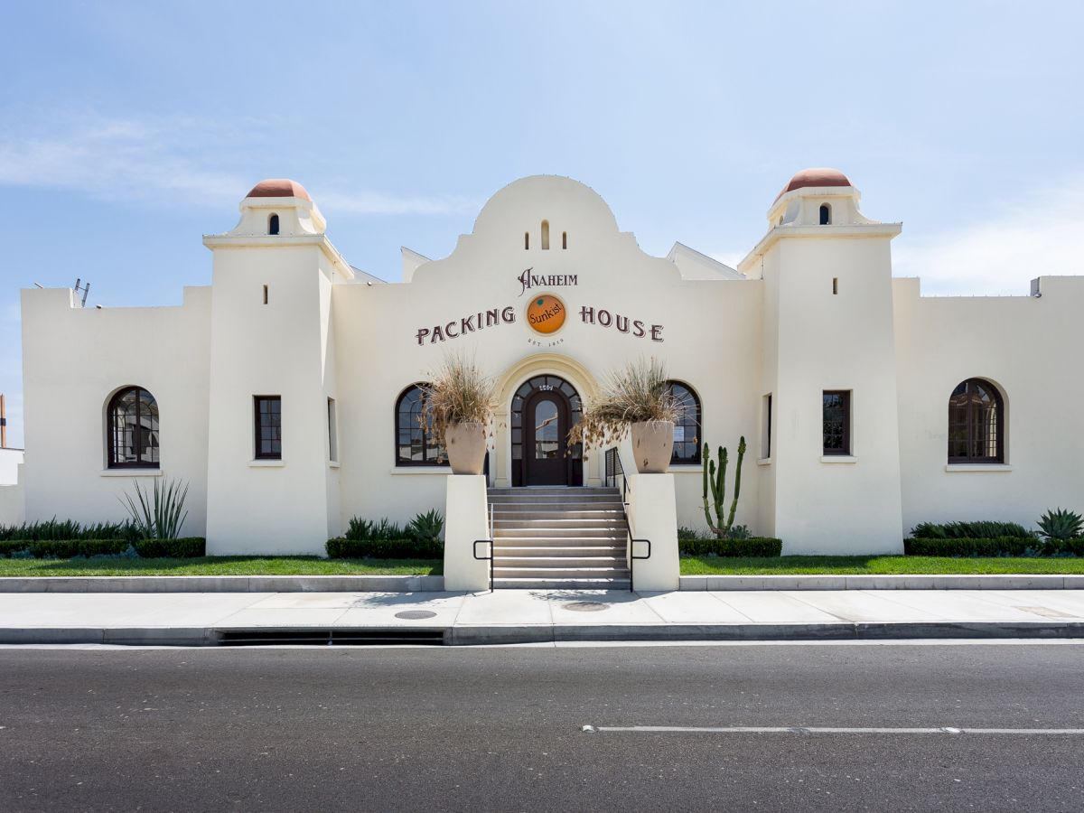 The image shows a white building with the words "Packing House" on it, featuring steps leading to the entrance and a clear sky in the background.