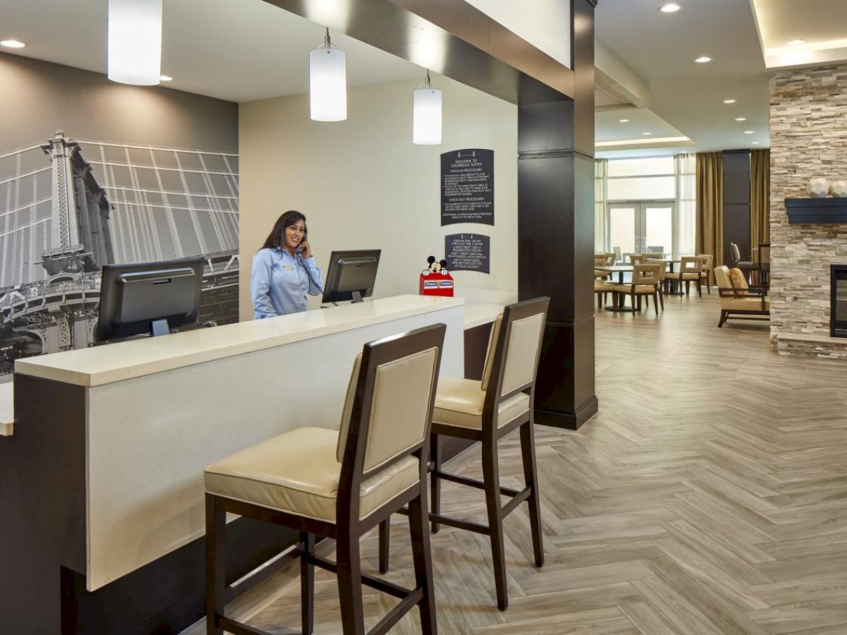 A reception area with a front desk, two chairs, and a receptionist. The space features modern decor, including a stone fireplace and a sitting area in the background.