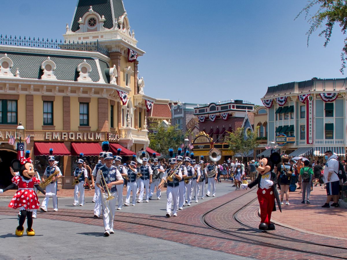 A parade at a theme park with performers in costume, including a marching band and characters in red and white polka-dotted and black outfits, entertains onlookers.