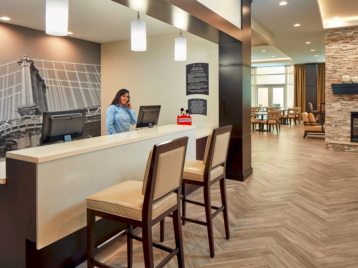 A person stands behind a reception desk in a modern lobby with a mural on the wall. The area has a seating section and a fireplace.