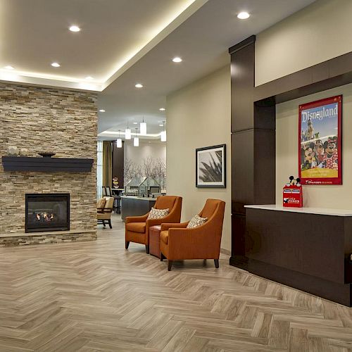 A modern lobby with a stone fireplace, brown chairs, framed pictures on walls, and recessed lighting on the ceiling.