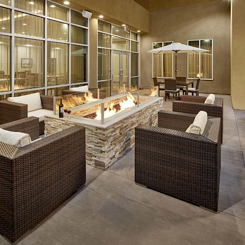 An outdoor patio with a fire pit, wicker seating, an umbrella table, and a barbecue grill is shown, creating a modern and cozy atmosphere.