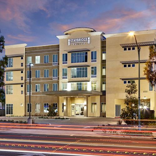 This image shows a modern, multi-story building with the sign "Residence Inn" on the front. Cars with light trails pass by on the street in front.