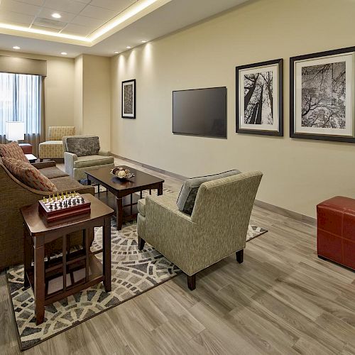 A modern living room with a seating area, wall-mounted TV, framed art, and a chess set on a small table, creating a cozy atmosphere.