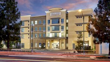 The image shows a multi-story building with "Staybridge Suites" signage, set along a street with light trails suggesting passing vehicles.