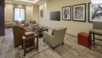 A modern living room features comfortable seating, a TV, framed artwork on the wall, a chess set on a side table, and hardwood flooring.