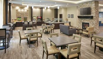 A modern, well-lit dining area with tables and chairs, a fireplace, and a self-serve food and beverage station in the background.