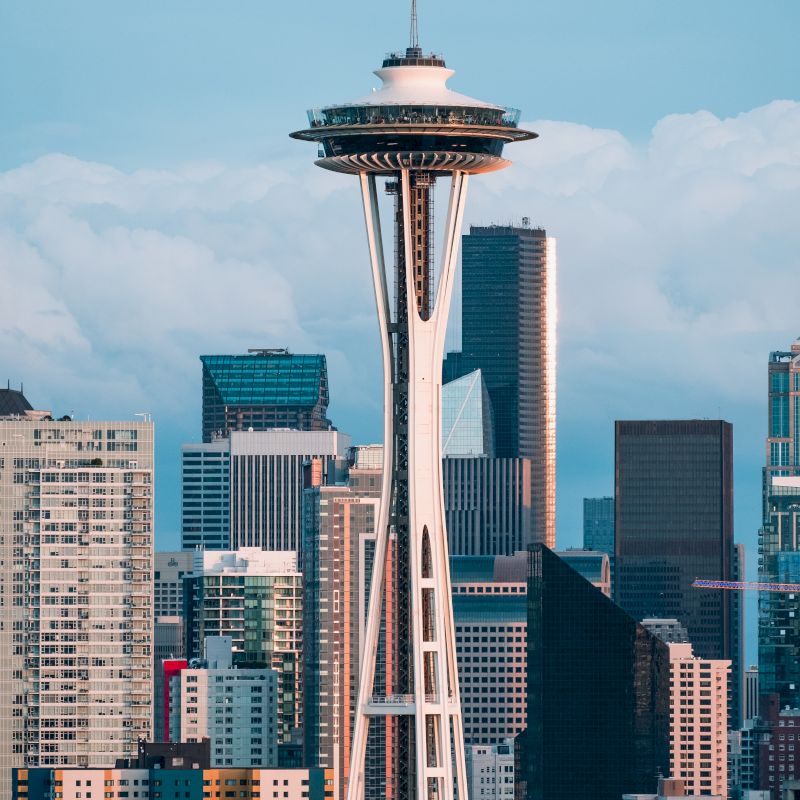 The image features the Space Needle with a backdrop of downtown Seattle buildings under a partly cloudy sky, capturing the city's iconic skyline.