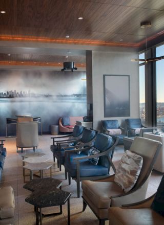 A modern lounge with comfortable seating, large windows with a view of a waterfront and Ferris wheel, and a mural of a city skyline on the wall.