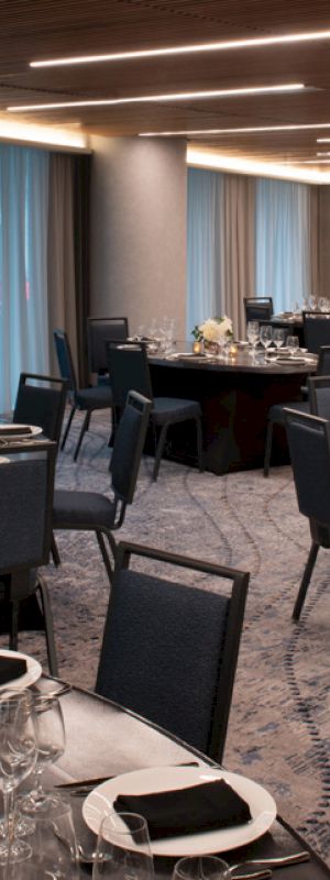 The image shows an elegantly set banquet hall with round tables and chairs, decorated with flowers, cutlery, and napkins, prepared for an event.