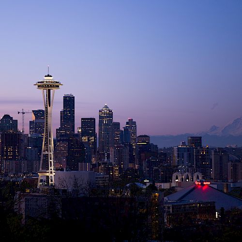 The image depicts the Seattle skyline at dusk, featuring the iconic Space Needle and Mount Rainier in the background, under a pastel-colored sky.