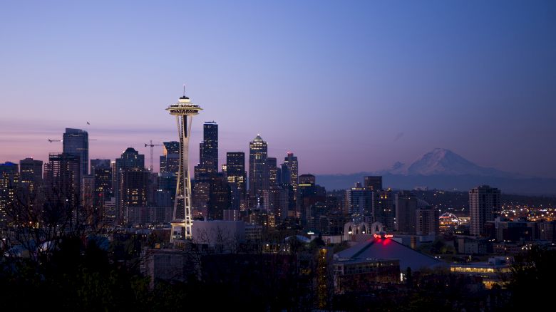 A twilight view of Seattle's skyline, featuring the iconic Space Needle, with Mount Rainier visible in the background.
