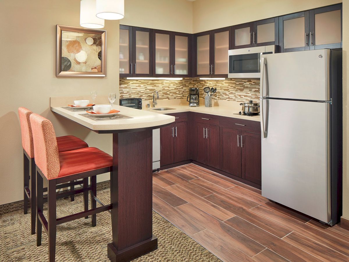 Modern kitchen with stainless steel appliances, dark cabinetry, and a counter with two bar stools. Artwork and pendant lights adorn the space.